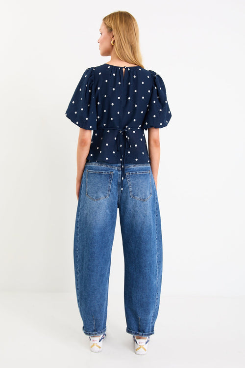 Model wearing a navy short sleeve bubble-sleeve top with white polka dots