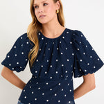 Model wearing a navy short sleeve bubble-sleeve top with white polka dots