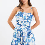 Woman wearing a blue floral mini dress with a pleated bodice, strappy sleeves, and a flattering fit, paired with white sandals.