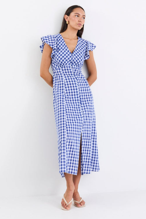 Woman wearing a blue gingham midi dress with a V-neck, button-down front, and fluted sleeves, paired with nude sandals.