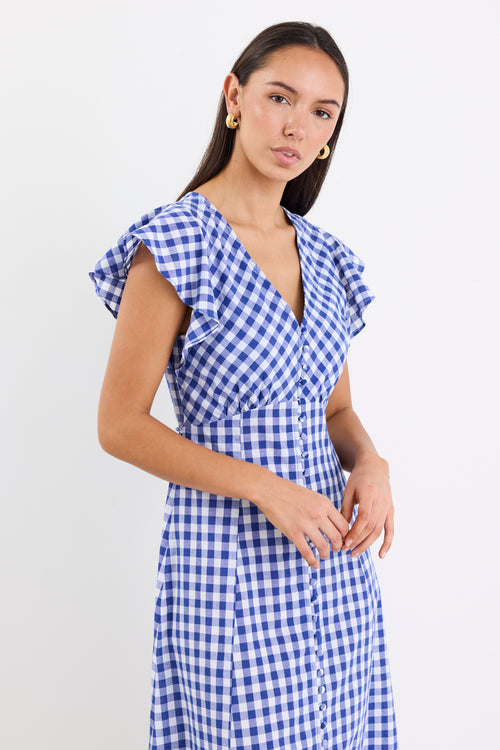 Woman wearing a blue gingham midi dress with a V-neck, button-down front, and fluted sleeves, paired with nude sandals.