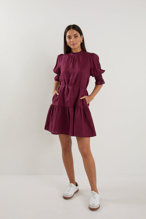 Woman wearing a short plum puff-sleeve mini dress with a tiered skirt, paired with white sneakers.