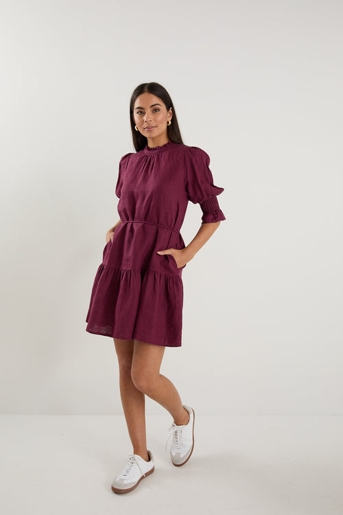 Woman wearing a short plum puff-sleeve mini dress with a tiered skirt, paired with white sneakers.