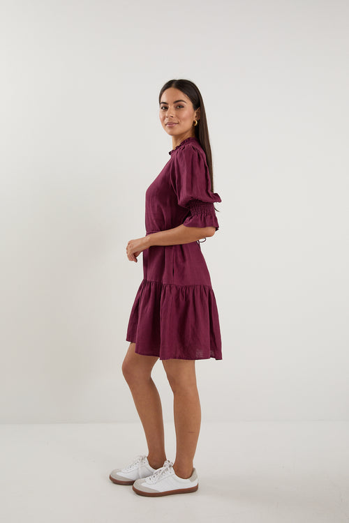 Woman wearing a short plum puff-sleeve mini dress with a tiered skirt, paired with white sneakers.