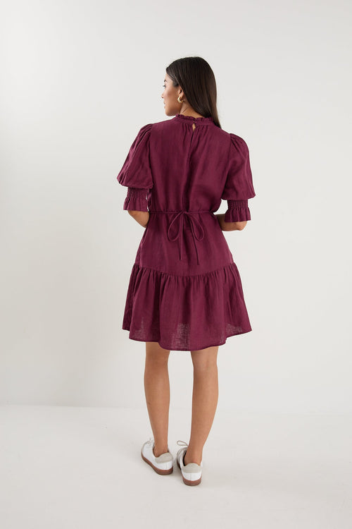 Woman wearing a short plum puff-sleeve mini dress with a tiered skirt, paired with white sneakers.