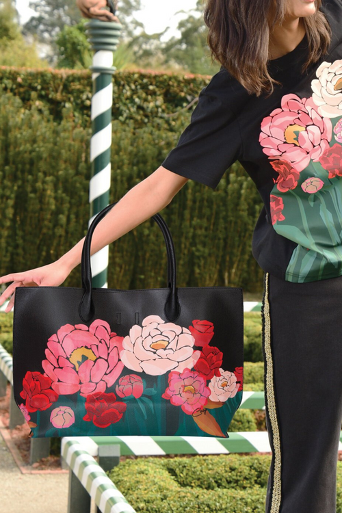 woman in a garden holding a black leather bag with pink and red roses printed onto it