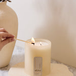 Hand lighting a candle with a decorative vase in the background