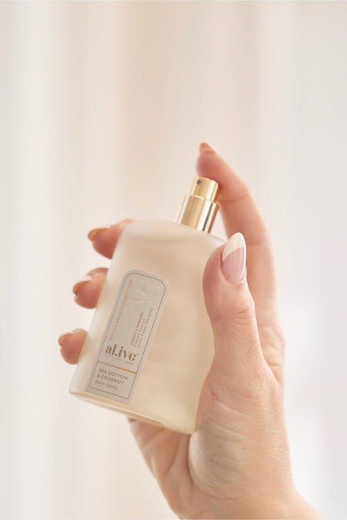 Hand holding a white bottle with a gold cap against a light background