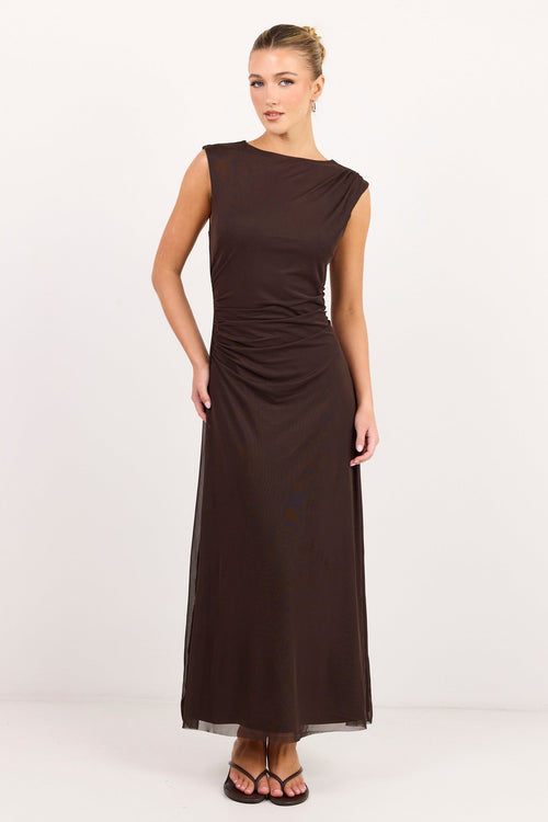 A woman modeling a sleeveless, dark brown maxi dress with a draped, gathered waist, standing against a plain white studio background.