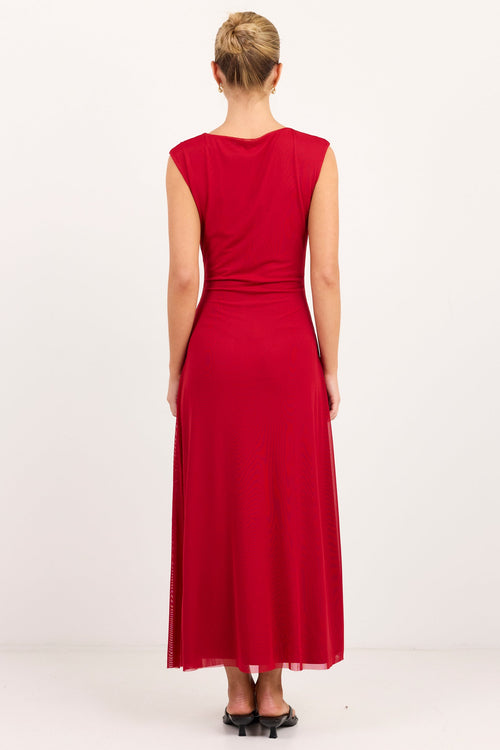 A woman viewed from the back wearing a sleeveless, floor-length red dress with a gathered waist, standing against a plain white studio background.