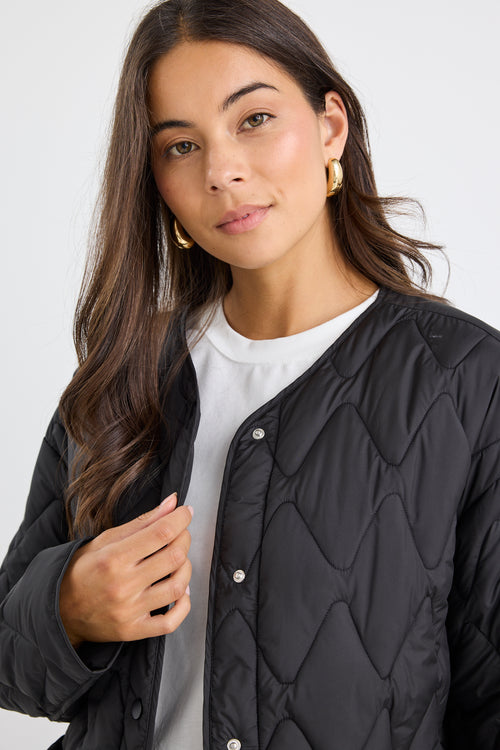 Woman wearing a black quilted jacket over a white shirt on a plain background