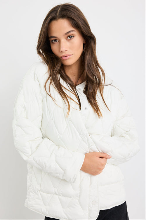 Woman wearing a white quilted jacket against a plain background