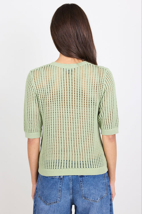 Woman wearing green knit tee and blue denim jeans on white background.