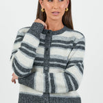 A woman wearing a striped knit cardigan in shades of grey and white with a button-down front, paired with dark blue high-waisted jeans.