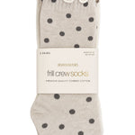 Three pairs of Stories by Tell frill crew socks in a light beige color with dark gray polka dots, packaged with a white paper band on a white background.