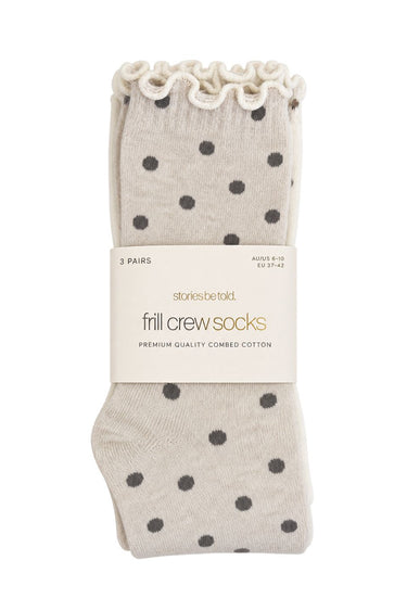 Three pairs of Stories by Tell frill crew socks in a light beige color with dark gray polka dots, packaged with a white paper band on a white background.