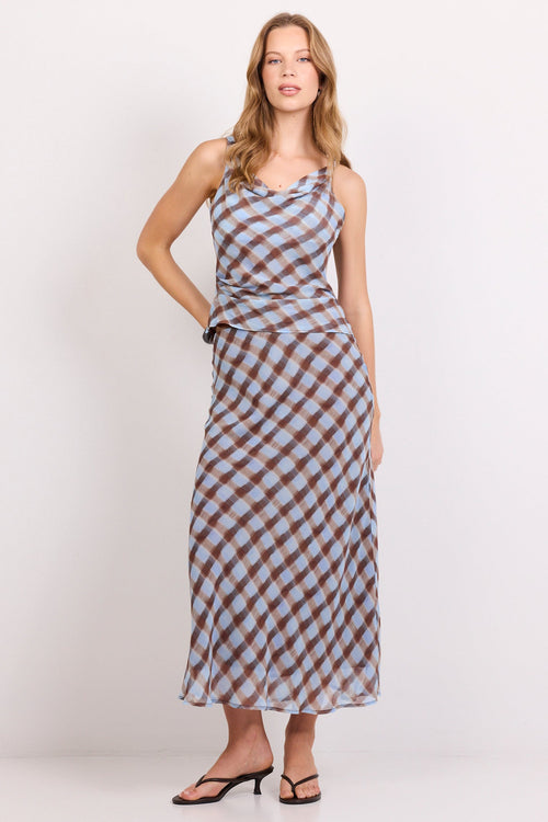 A woman modeling a sleeveless maxi dress with a brown and light blue checkered pattern, standing against a plain white studio background.