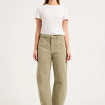 A woman modeling a pair of high-waisted, wide-leg olive green trousers, styled with a white t-shirt and light pink sandals against a plain white studio background.