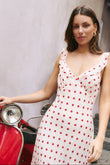 Woman in a white dress with red polka dots standing next to a red scooter.