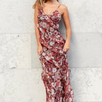 Woman in a floral dress standing against a light gray wall.