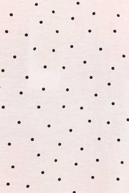 A close-up of a light cream fabric with a scattered pattern of small black polka dots.