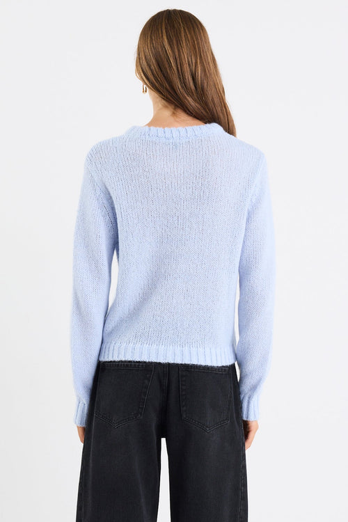 Person wearing a light blue sweater and black pants on a white background