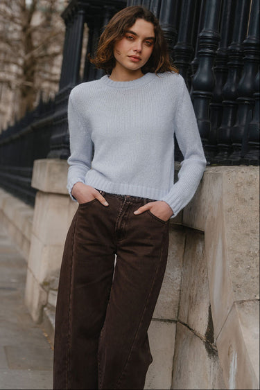 Woman in a light gray sweater and brown pants standing against a black iron gate.
