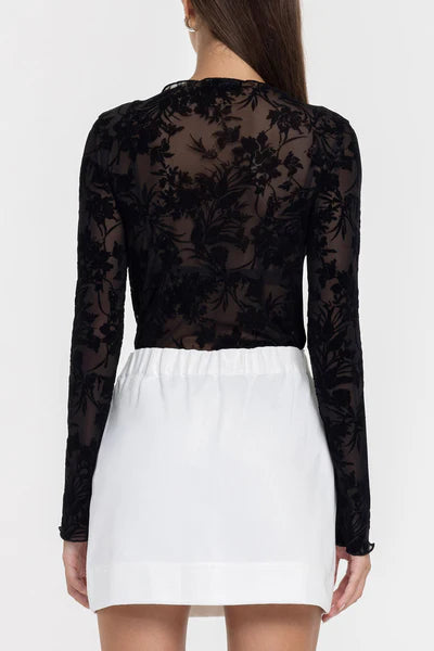 Black floral lace top with long sleeves and a white skirt on a white background