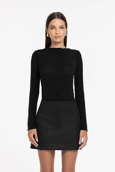 Woman wearing a black long-sleeve top with a pattern and a black skirt on a white background