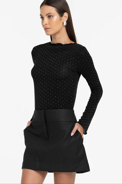 Woman wearing a black long-sleeve top with white polka dots and a black skirt on a white background