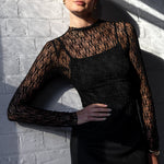 Person wearing a black lace top against a white brick wall