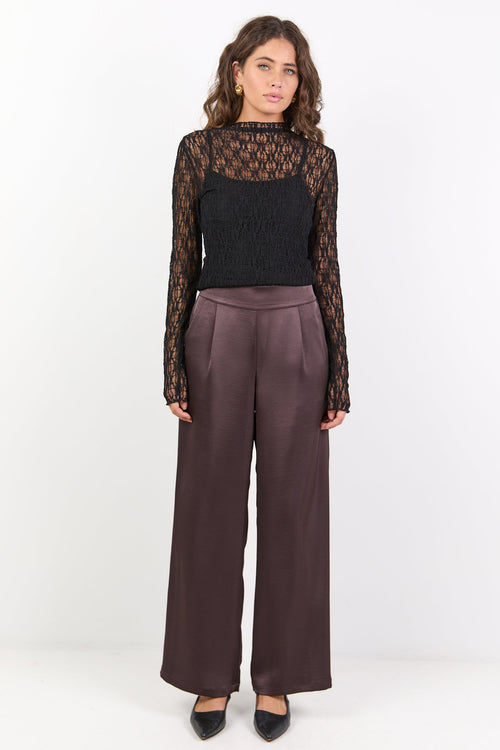 Woman wearing a black lace top and brown pants on a white background