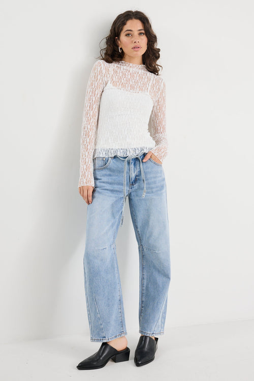 Woman wearing a patterned sweater, white shirt, blue jeans, and black shoes on a white background