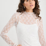 Woman wearing a white lace top and denim shorts on a plain background