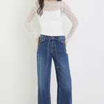 Woman wearing a white top with lace sleeves and blue jeans on a white background