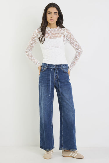 Woman wearing a white top with lace sleeves and blue jeans on a white background