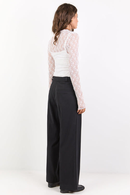 Woman wearing a white lace top and black wide-leg pants on a white background