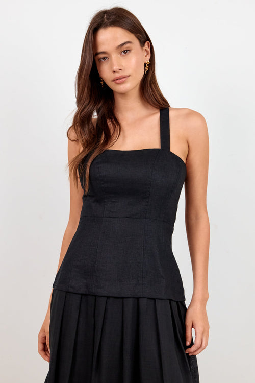 A woman modeling a black sleeveless midi dress with a structured bodice, square neckline, wide shoulder straps, and a flowing skirt, photographed against a plain light gray studio background.