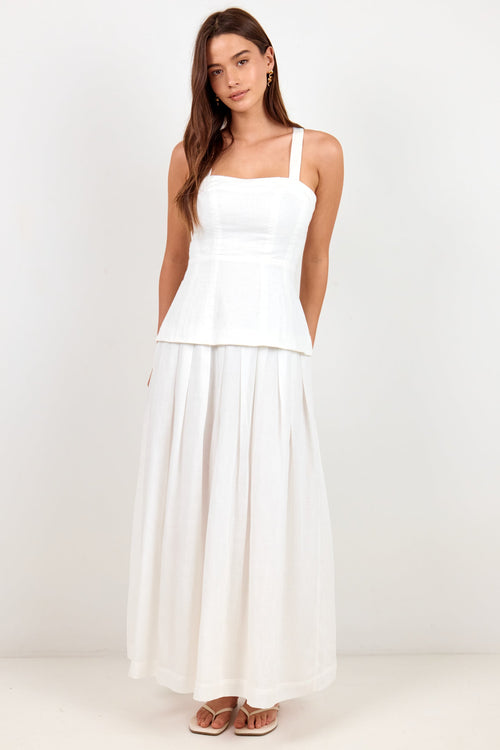 A woman modeling a white sleeveless maxi dress with a structured peplum waist and a flowing skirt, standing against a plain white studio background.