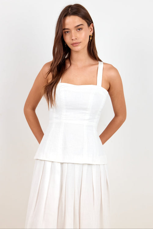 A woman modeling a white sleeveless peplum-style top and matching white skirt against a plain light background.