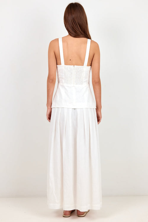 A woman viewed from behind wearing a white sleeveless maxi dress with a structured corset-style bodice and a flowing skirt, standing against a plain white studio background.