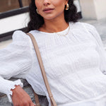 model wears a white cotton long sleeve top with blue jeans and a brown handbag