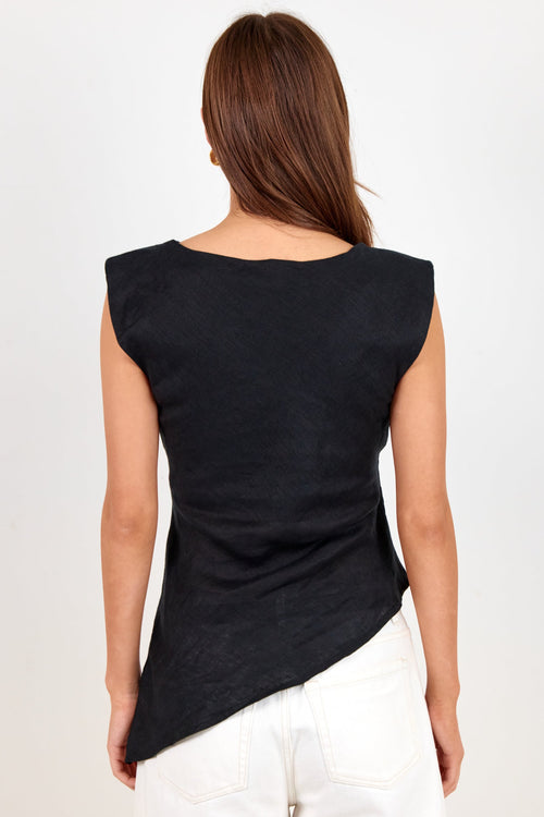 A woman viewed from the back wearing a black sleeveless top with an asymmetrical hem and white pants, set against a plain light background.