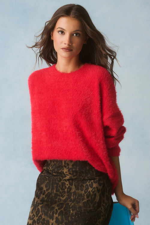 Woman wearing a red sweater and leopard print skirt against a light blue background