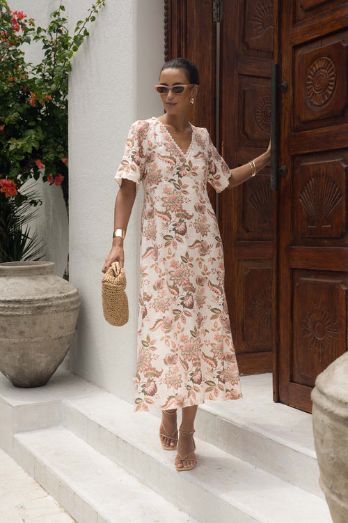 Woman in a floral dress standing in front of a wooden door with decorative carvings.