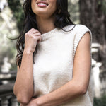Woman wearing a cream sleeveless sweater and red skirt outdoors