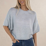 Woman wearing a light blue knitted sweater and jeans against a beige background