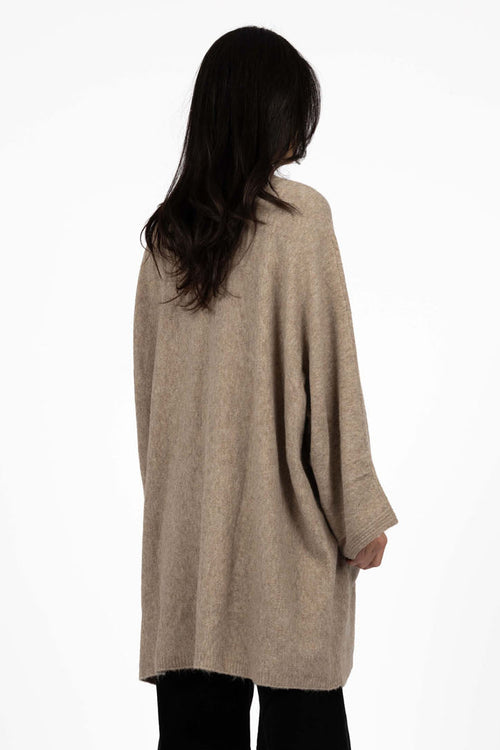 Person wearing a beige cardigan and black pants on a white background