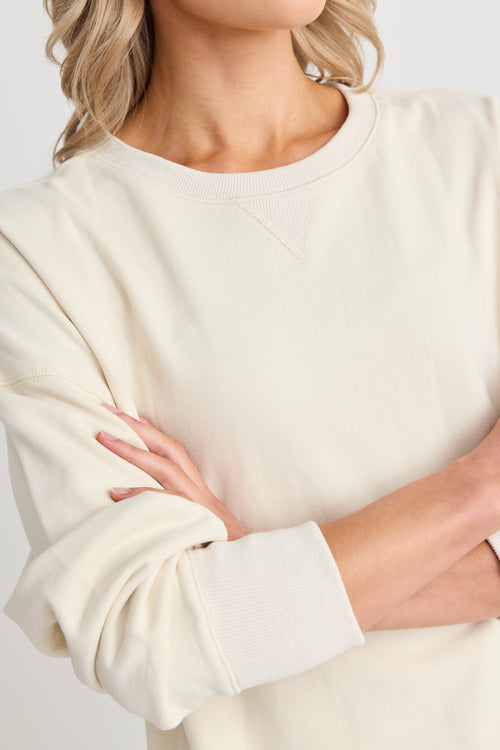 Model wears a cream sweatshirt and black shorts