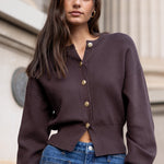 Woman wearing a brown cardigan and blue jeans standing in front of classical architecture.